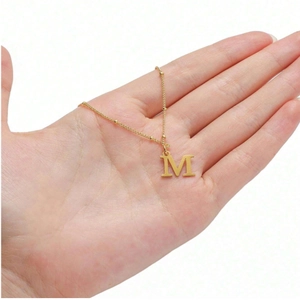 Detail of a minimalist gold necklace with a capital letter M pendant held in hand