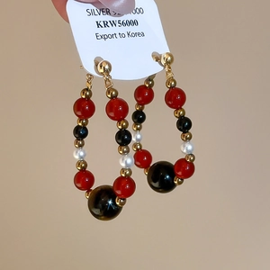 Detail of beaded hoop earrings with red, black and white pearls on golden metal hooks