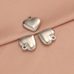 Close-up of three polished silver heart-shaped stainless steel pendants on pink fabric