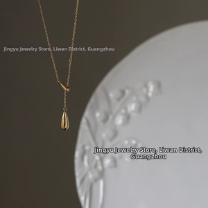 Detailed macro shot of a golden double teardrop pendant necklace on white floral porcelain