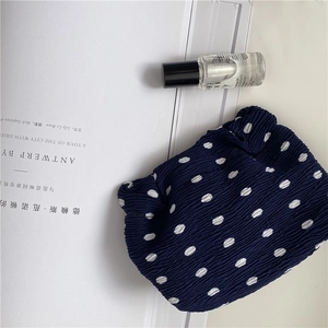 Flat lay of navy blue polka dot chiffon makeup bag with skincare bottle and magazine