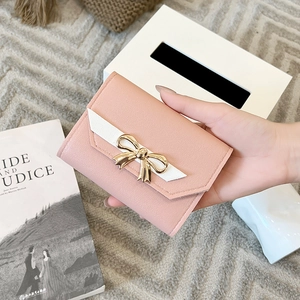 Detail of pink PU leather wallet with white trim and gold bow accent held by hand