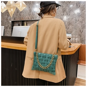 Detail of green woven crossbody bag featuring a chunky gold chain strap in a cafe setting