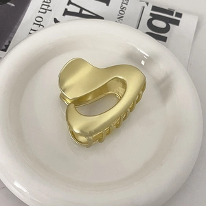 Detail of matte gold heart-shaped metal hair claw clip displayed on a white plate