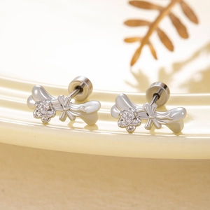 Cute silver bone and floral stud earrings with tiny gemstones on a ceramic plate