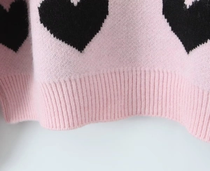 Close-up of pink knit sweater ribbed hem with black heart pattern details