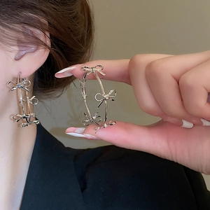 Close-up of silver hoop earrings featuring four 3D metallic bows in elegant French style