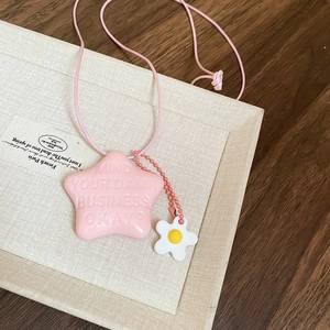 Dettaglio del ciondolo a stella rosa con slogan inciso e charm a fiore sulla collana