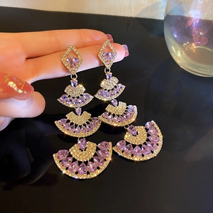 Macro view of gold fan earrings with purple zircons and rhinestones for evening wear