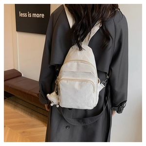 Dettaglio di uno zaino in nylon beige con trama a pieghe, ciondolo e cerniera dorata