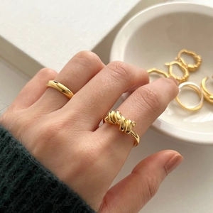Close-up of a 925 sterling silver knot ring and smooth gold band on a hand