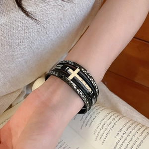 Gros plan du bracelet en cuir tressé multicouche avec pendentif croix argenté sur poignet