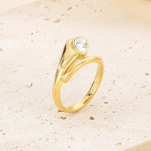 Macro detail of gold snake ring featuring a teardrop crystal on beige stone surface