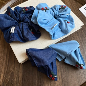 Detailed close-up of blue fabric scrunchies with cherry embroidery and white pearls