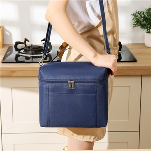 Navy blue thermal lunch bag with adjustable shoulder strap shown in a kitchen setting