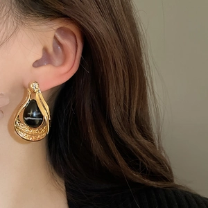 Close-up of vintage gold teardrop earring with black faux agate worn by a model