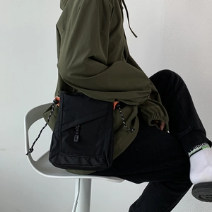 Close-up of black nylon crossbody bag with drawstring detail worn by a sitting model