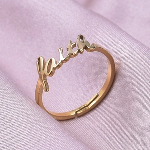 Detail of adjustable gold stainless steel ring with cursive faith lettering on pink satin