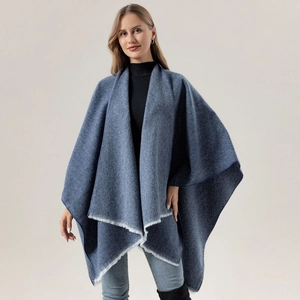 Blue solid color shawl poncho with white fringe edges worn by a female model with boots
