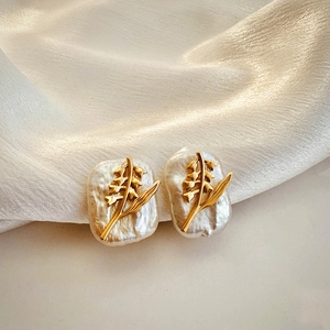 Detail of golden floral leaf studs with baroque pearls on soft silk background