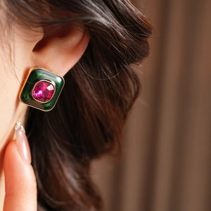 Detail view of vintage gold earrings with dark green enamel and a pink gemstone inlay