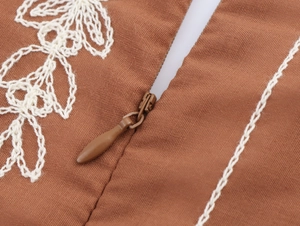 Détail macro de broderie florale blanche et fermeture éclair invisible sur tissu marron