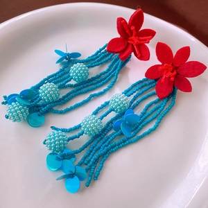 Detail of red flower studs and sky blue beaded fringe tassels on bohemian earrings
