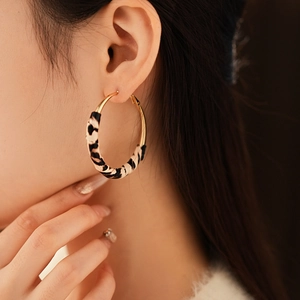 Gros plan de boucles d'oreilles créoles dorées en cuir léopard portées par un mannequin