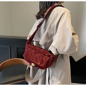 Close-up of quilted burgundy saddle bag with gold swivel clasp and adjustable strap