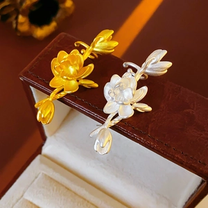 Detailed close-up of gold and silver metal lotus earrings on a brown leather texture box