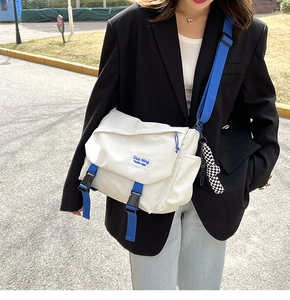White nylon messenger bag with blue straps shown on a model in an outdoor setting