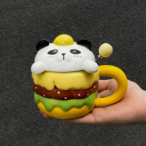 Close-up of ceramic hamburger mug with panda lid and yellow spoon held in hand