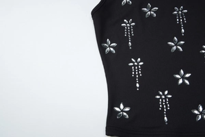 Détail du débardeur noir côtelé avec fleurs argentées et décorations de strass à franges