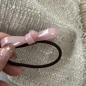 Detailed view of a pink bow hair tie held by a hand over a beige woven background