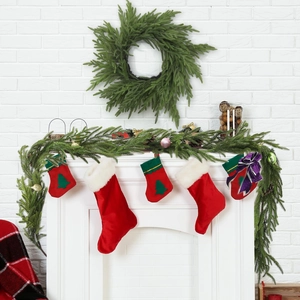 Artificial Norfolk Pine garland and wreath with Christmas stockings on a fireplace