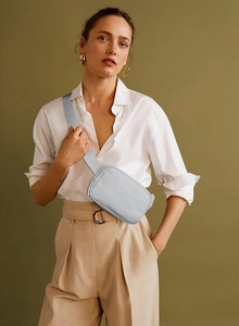 Close-up of a light blue waterproof belt bag worn as a crossbody on a white shirt