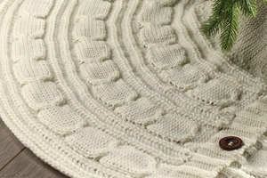 Detail of cable knit Christmas tree skirt with wooden buttons on dark wood floor