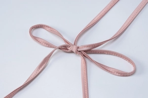 Dettaglio di un abito in raso rosa con spallina a fiocco e texture di seta pregiata