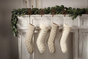 Detail of four knit Christmas stockings with fish scale pattern hanging on a white fireplace