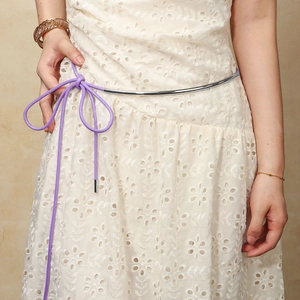 Detail of silver metal half-ring and purple wax cord belt tied on a white lace dress