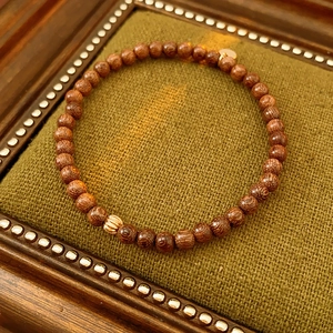 Close-up of brown wooden bead bracelet with a gold metal bead in a vintage green box