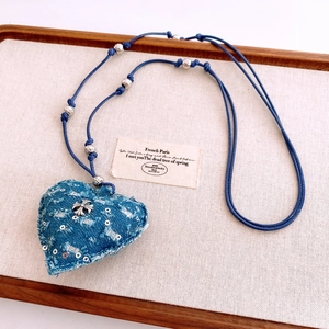 Détail d'un pendentif cœur en denim bleu avec perles argentées et croix sur cordelette