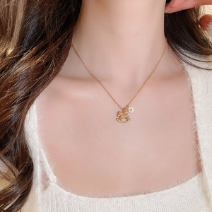 Detail of a gold plated necklace with a small horse pendant worn on a white sweater