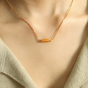 Minimalist gold geometric twisted bar necklace shown on a model with a beige knit top