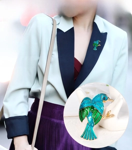 Detailed close-up of a blue and green enamel bird brooch worn on a light suit lapel