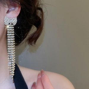 Close-up of sparkling bow tassel earrings with long rhinestones on a female model