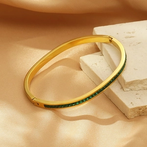 Détail du bracelet ovale doré orné de zircons verts sur un fond en soie élégant