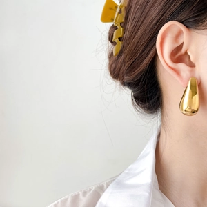 Detail of hollow golden water drop earrings with a polished mirror finish on model