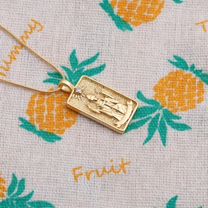 Detail of gold geometric necklace pendant featuring embossed figure and zircon inlay