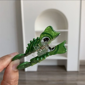 Close-up of a cute emerald green dinosaur hair claw clip with golden metal spring